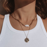 Model wearing 18k gold layered necklace with a pearl and roman coin. Waterproof and tarnish-resistant design.