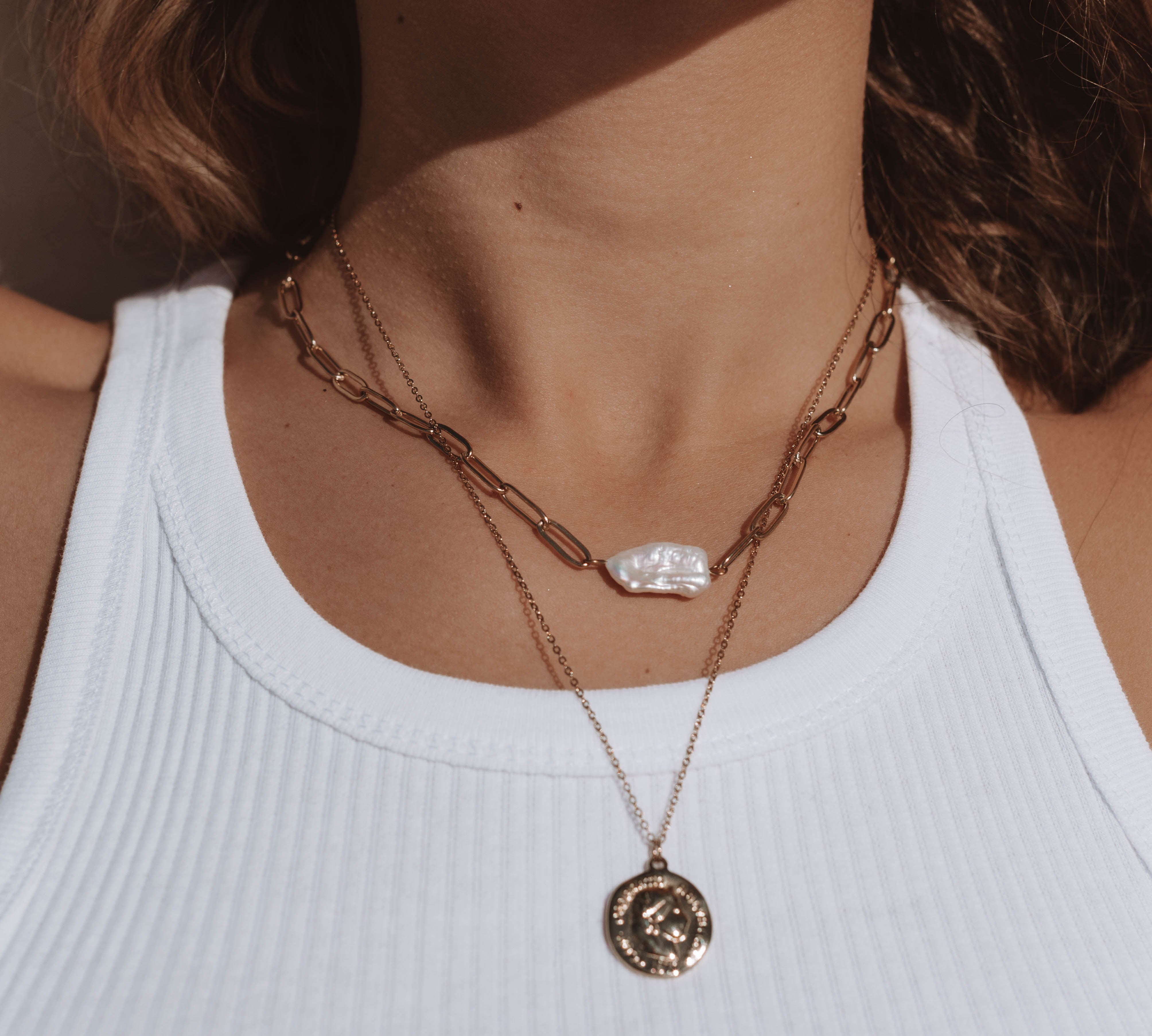 Model wearing 18k gold layered necklace with a pearl and roman coin. Waterproof and tarnish-resistant design.