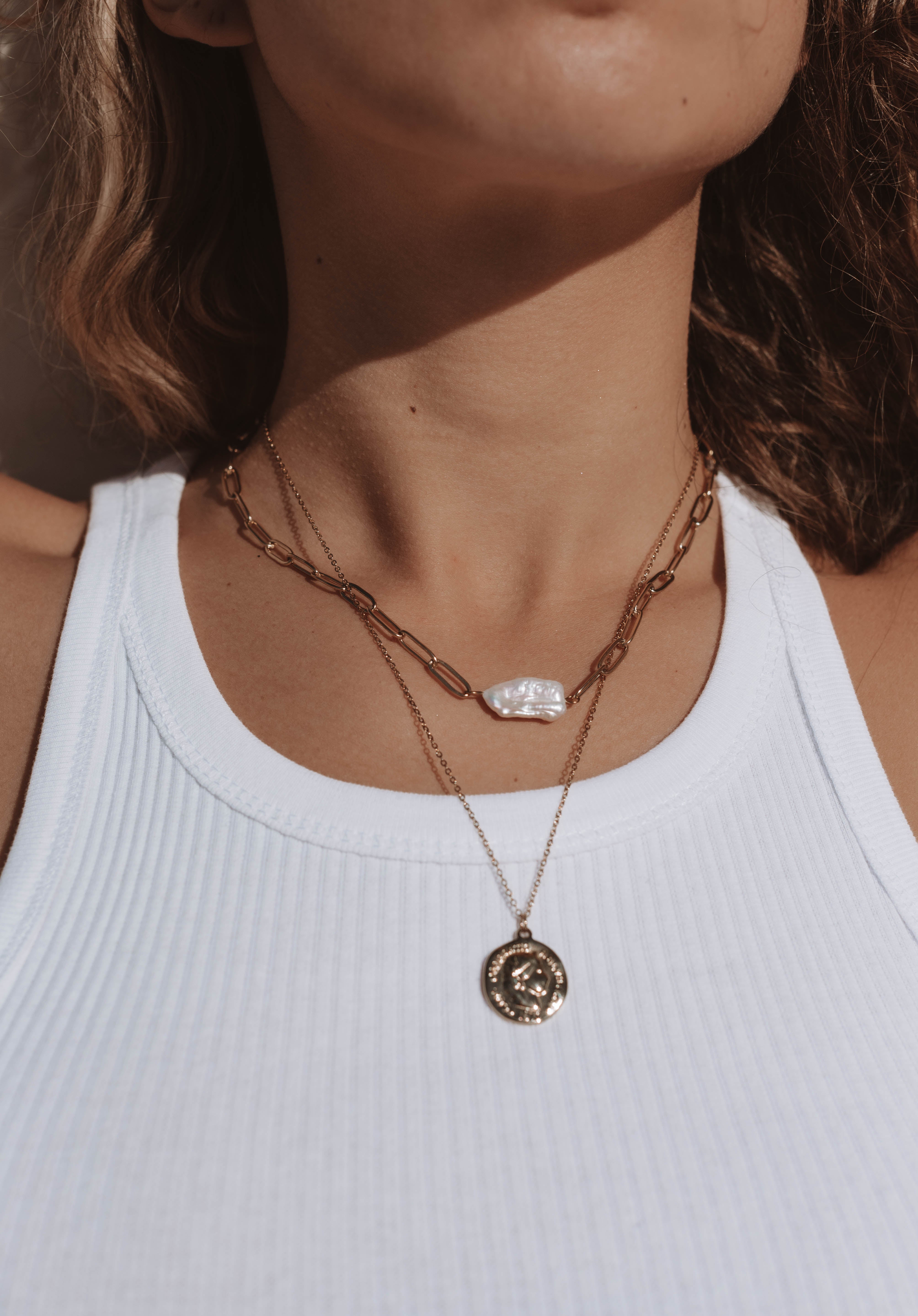 Model wearing 18k gold layered necklace with a pearl and roman coin. Waterproof and tarnish-resistant design.