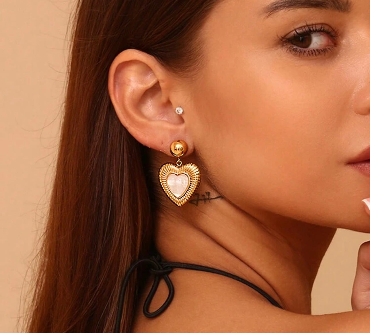 Model wearing 18k gold heart-shaped earrings featuring a mother of pearl inner layer, designed to be hypoallergenic and waterproof