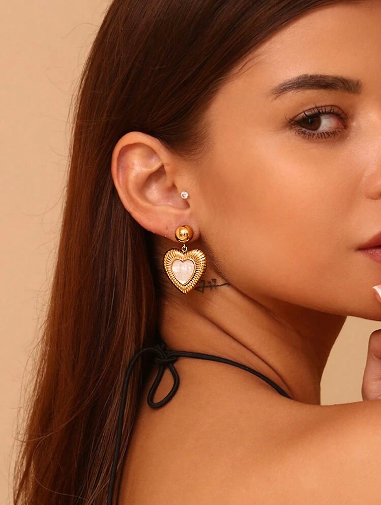 Model wearing 18k gold heart-shaped earrings featuring a mother of pearl inner layer, designed to be hypoallergenic and waterproof