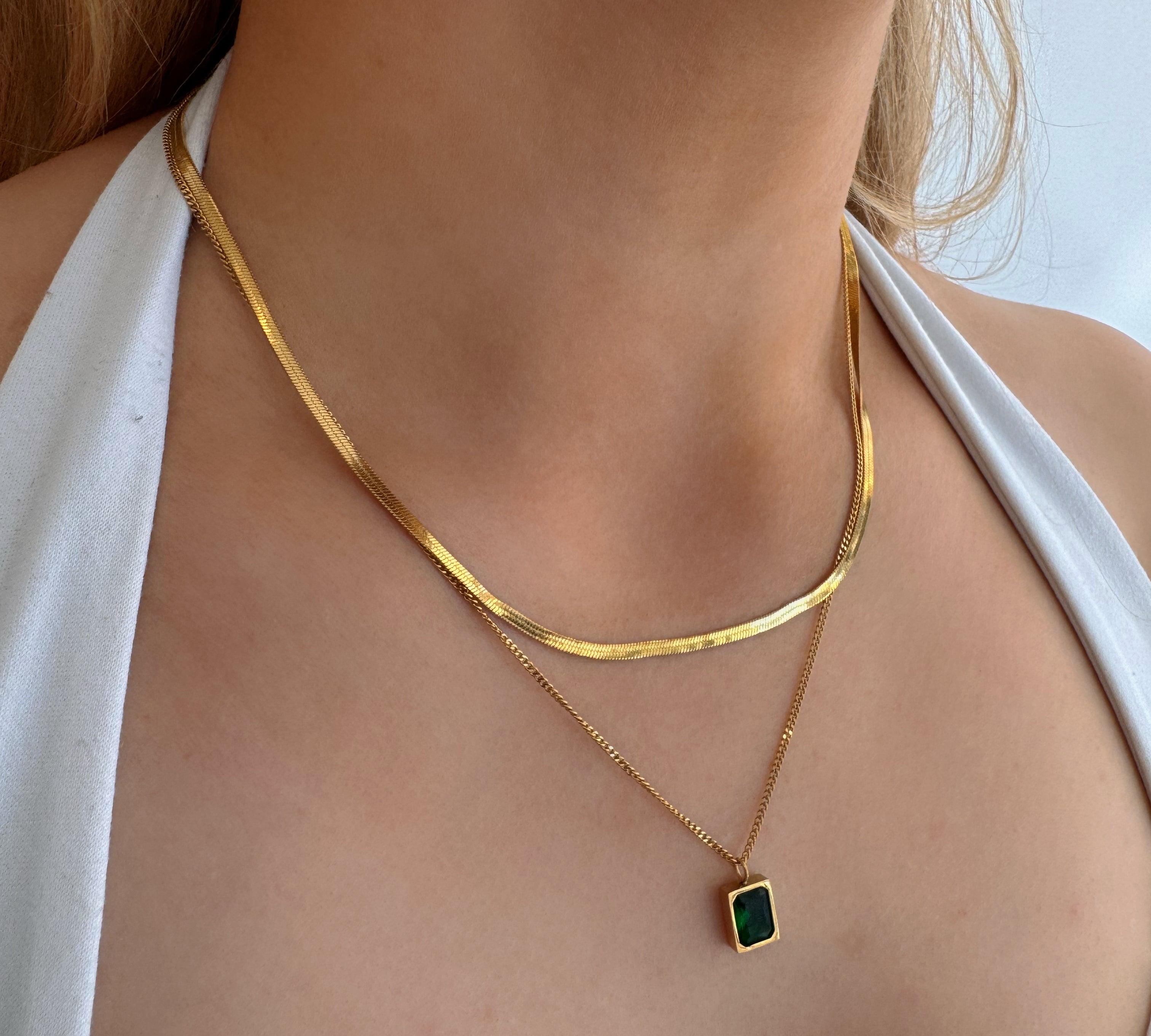 model wearing 18k gold layered necklace featuring a emerald colour designed to be waterproof and hypoallergenic for everyday wear.