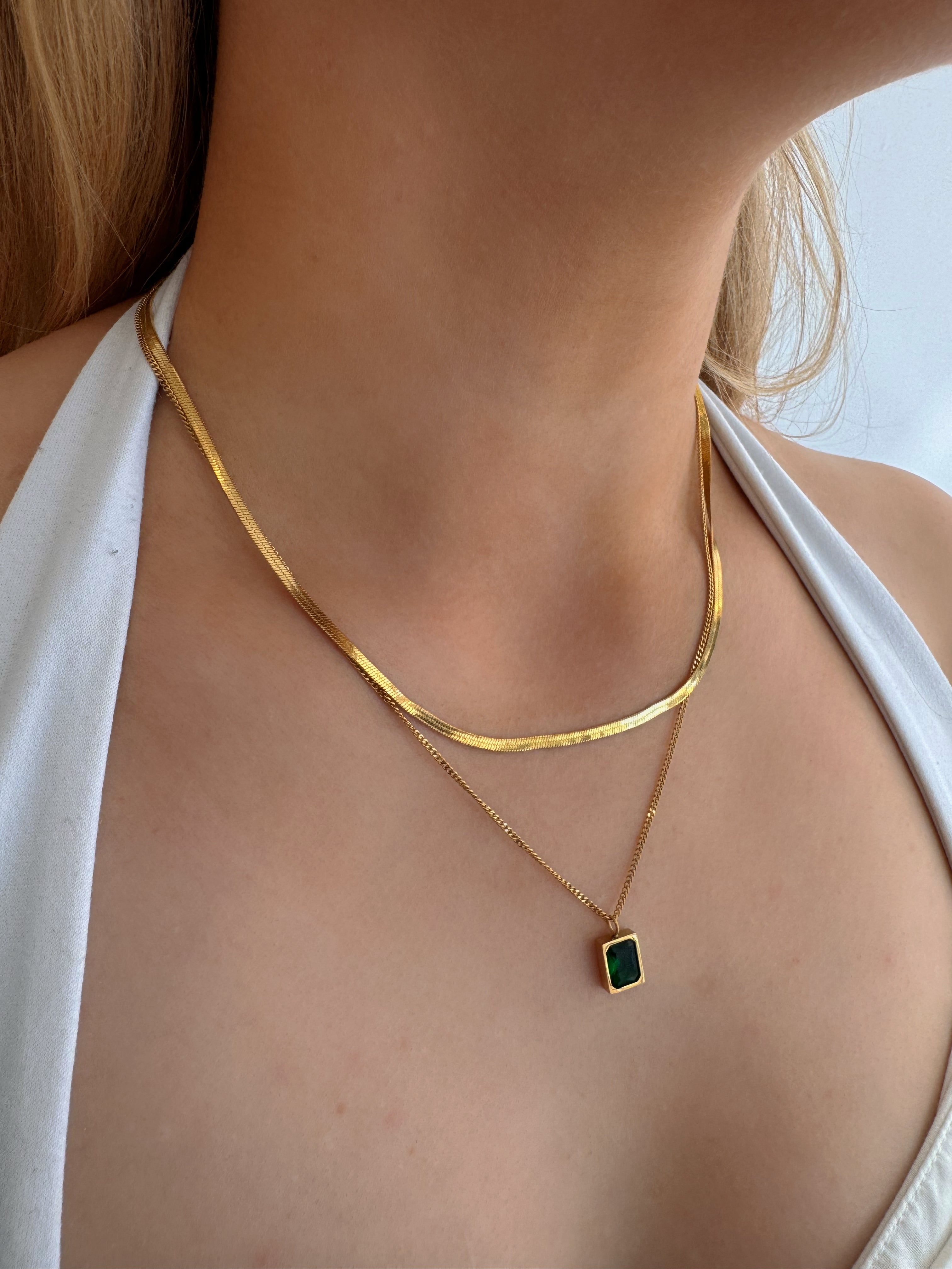 model wearing 18k gold layered necklace featuring a emerald colour designed to be waterproof and hypoallergenic for everyday wear.