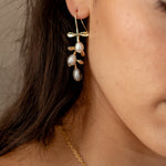 Model wearing gold hook earrings featuring tiered drop leaves adorned with three pearls, adding a touch of elegance and nature-inspired charm