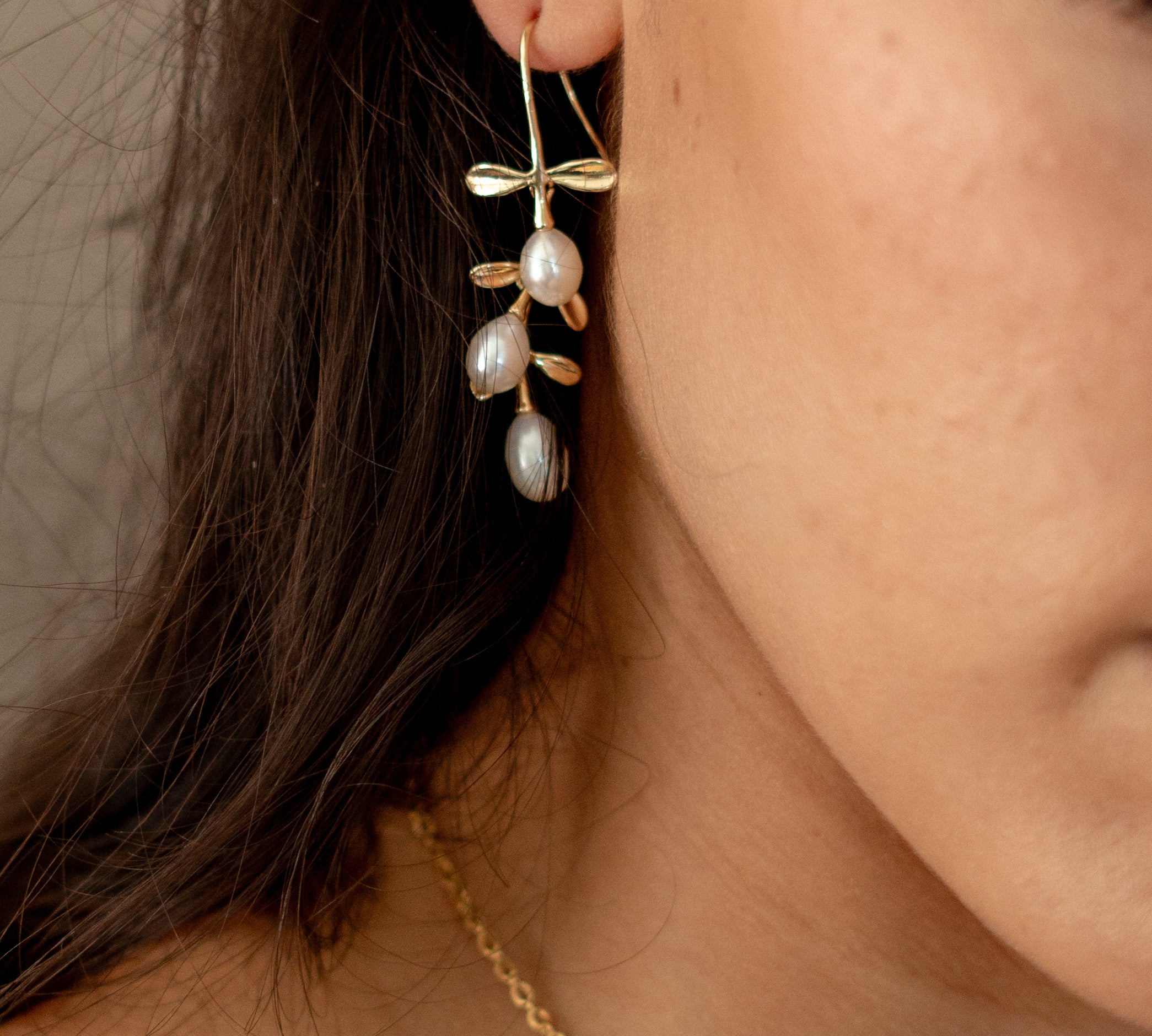 Model wearing gold hook earrings featuring tiered drop leaves adorned with three pearls, adding a touch of elegance and nature-inspired charm