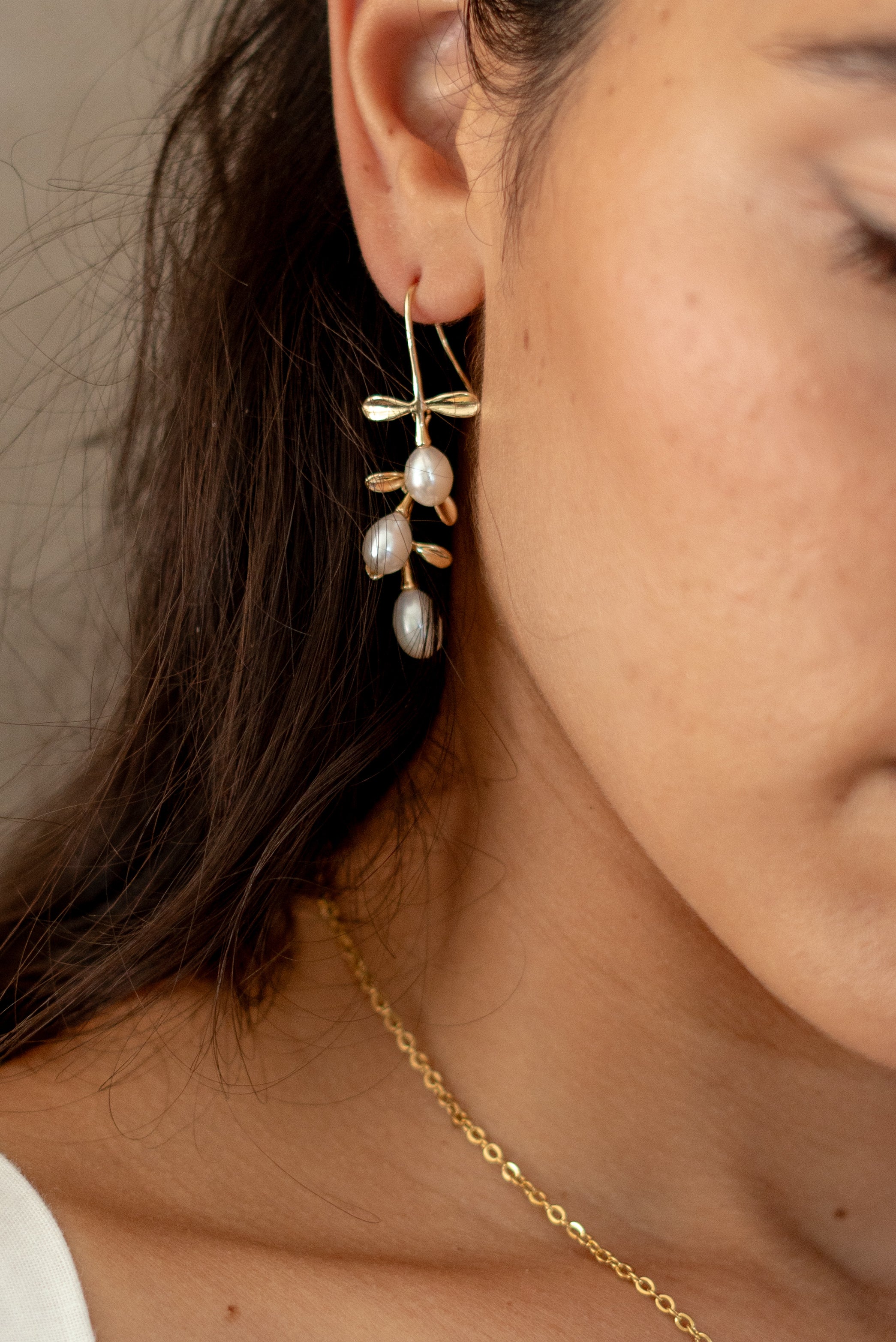 Model wearing gold hook earrings featuring tiered drop leaves adorned with three pearls, adding a touch of elegance and nature-inspired charm