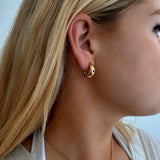 Model wearing small hoop earrings with three stars adorned with multi-coloured stones, featuring scalloped edging, designed to be waterproof and hypoallergenic