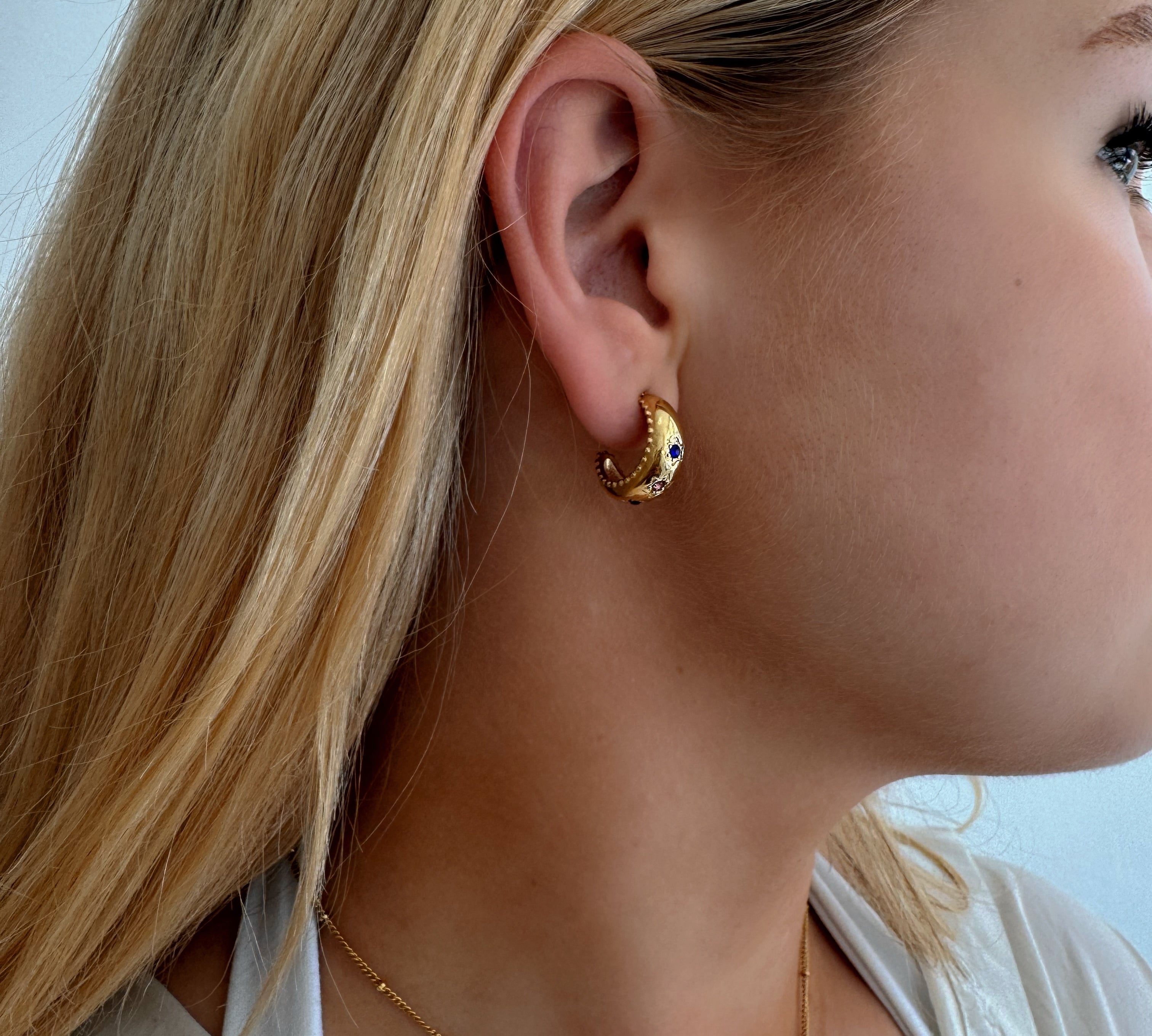 Model wearing small hoop earrings with three stars adorned with multi-coloured stones, featuring scalloped edging, designed to be waterproof and hypoallergenic