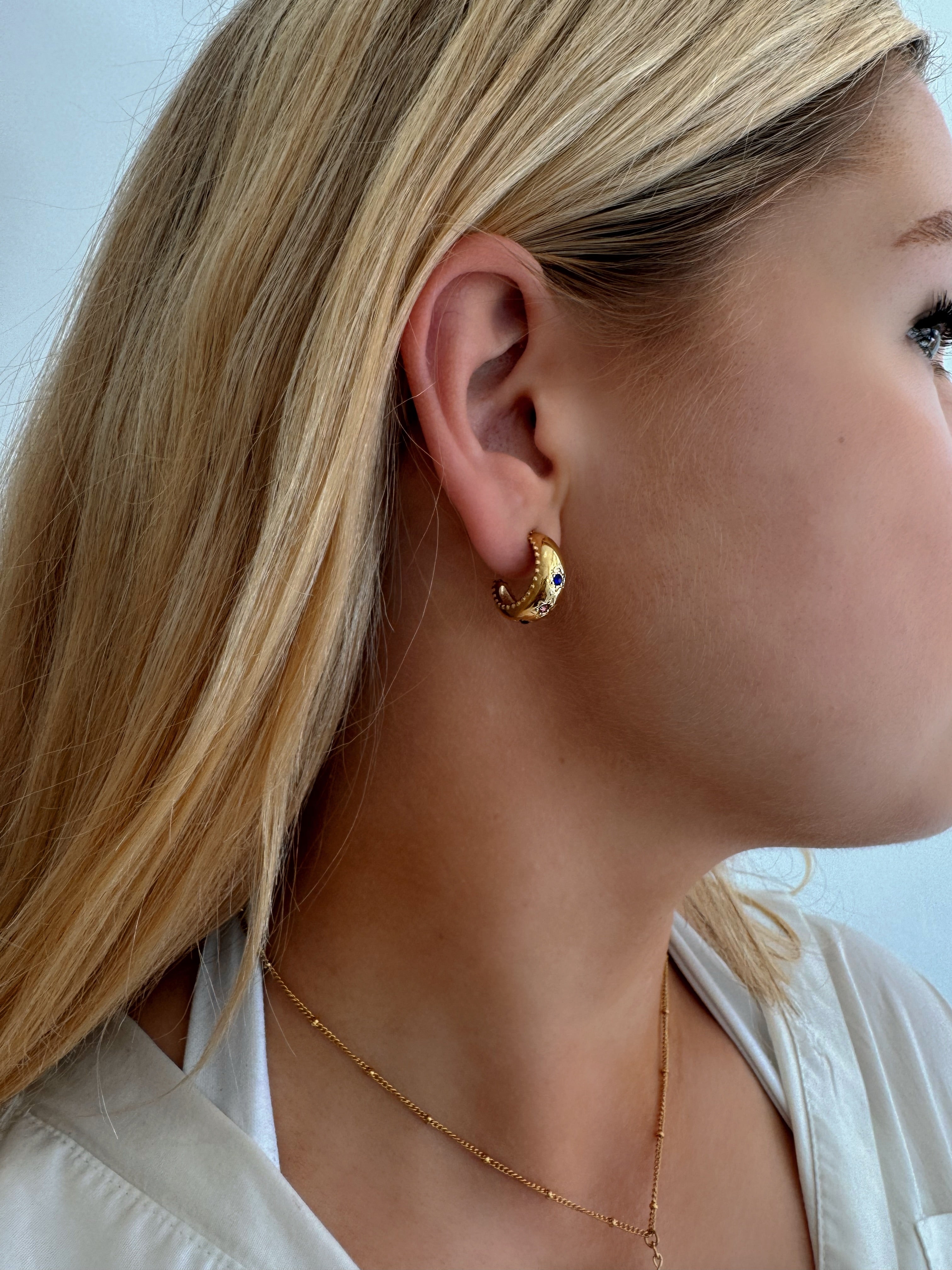 Model wearing small hoop earrings with three stars adorned with multi-coloured stones, featuring scalloped edging, designed to be waterproof and hypoallergenic