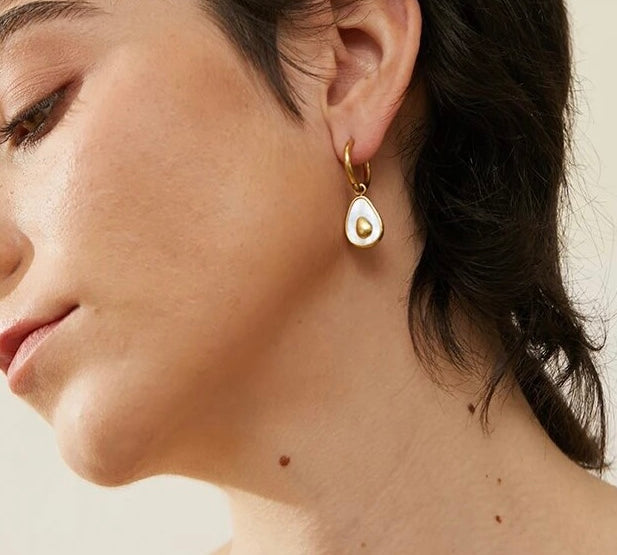 Model wearing 18k gold avocado earrings with a mother of pearl inner, designed to be hypoallergenic and tarnish-resistant for lasting wear