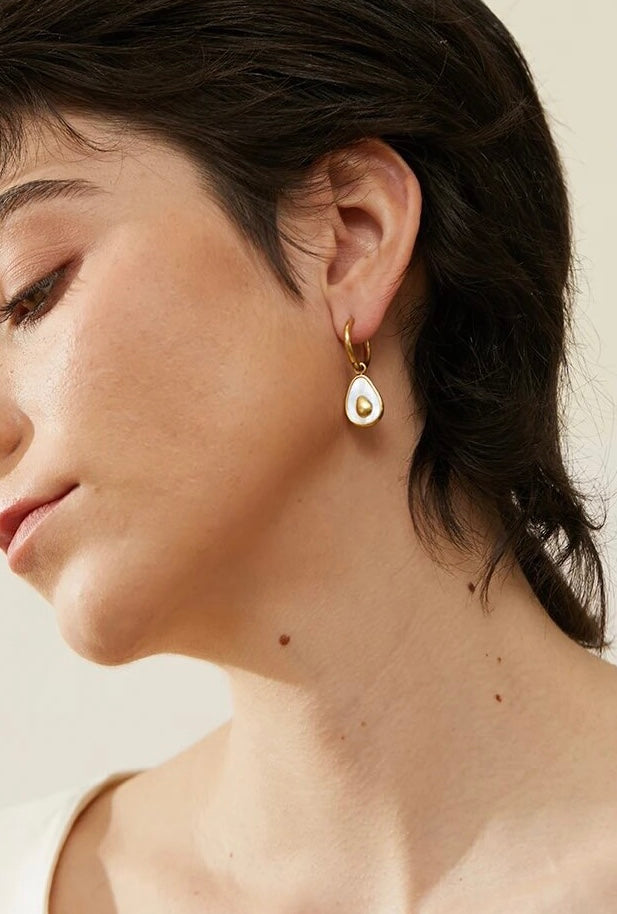 Model wearing 18k gold avocado earrings with a mother of pearl inner, designed to be hypoallergenic and tarnish-resistant for lasting wear