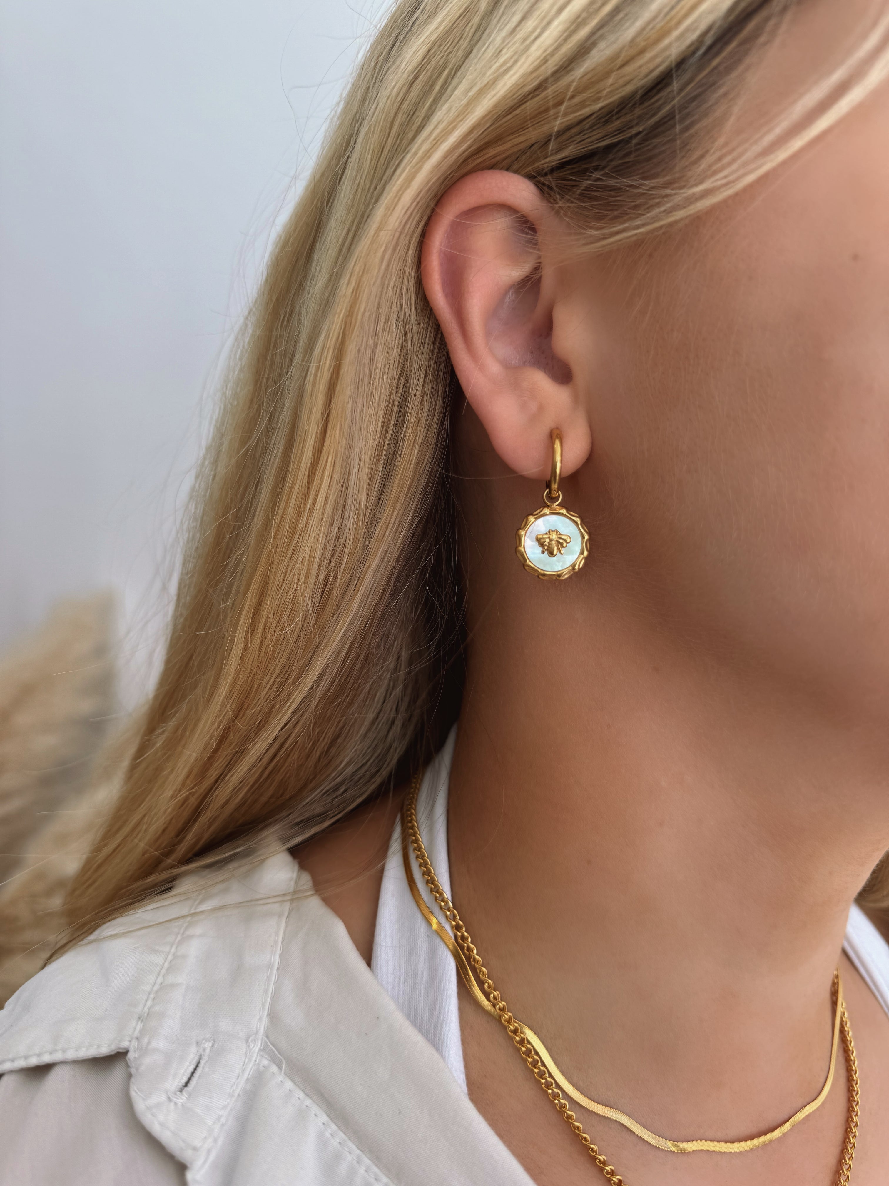 model wearing 18k gold mother of pearl coin earrings featuring a bee motif and a removable pendant, allowing for two styling options. Waterproof, hypoallergenic, and tarnish-resistant