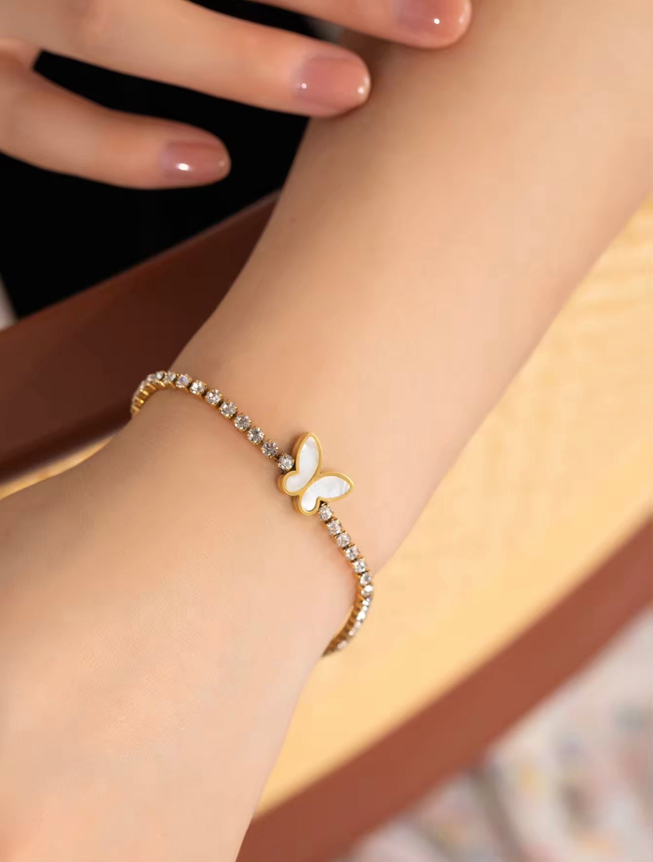 Model wearing 18k gold tennis bracelet featuring a butterfly and flower design with mother of pearl and high-quality cubic zirconia, crafted to be tarnish-resistant for enduring elegance